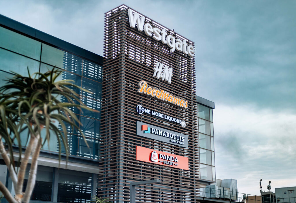 Shopping centre exterior with a tall sign displaying logos for Westgate, RoccaMamas, One More Liquor, Panarottis, and Panda, against a cloudy sky. - Pareto Limited