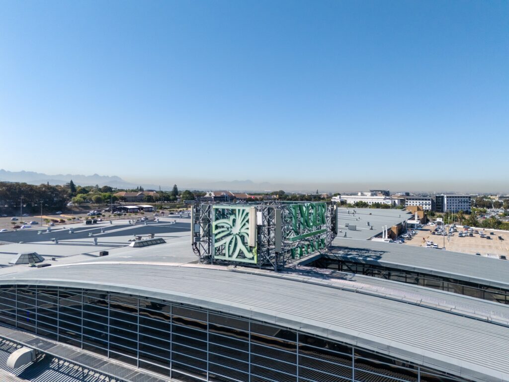 A large rooftop air conditioning unit with green and white panels sits atop a modern industrial building, typical of those found in Pareto portfolio shopping centres, under a clear blue sky. - Pareto Limited