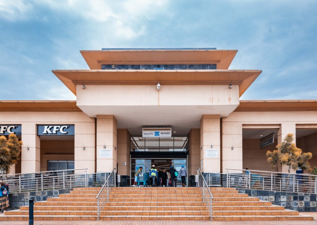 Wide view of a modern building entrance at Westgate Mall Roodepoort, with steps leading up, people entering, and KFC signs visible on both sides. - Pareto Limited